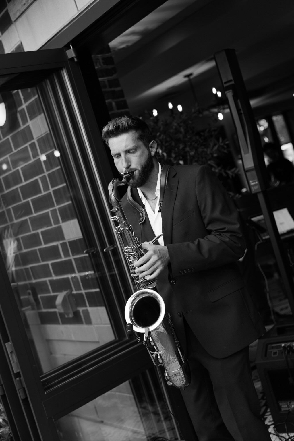 Dawson Bertrand playing baritone saxophone in a suit at an upscale cocktail event, black and white