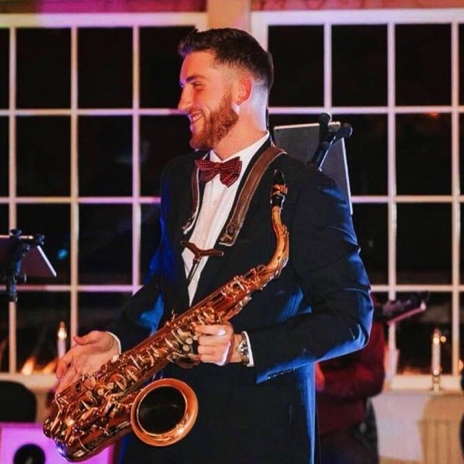 Dawson Bertrand smiling in a tuxedo and bow tie with tenor saxophone at a wedding reception