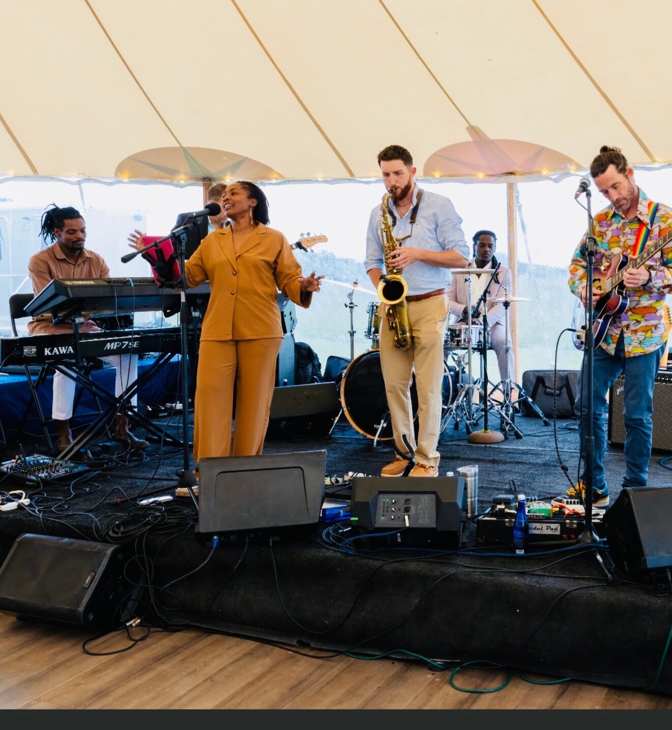 Dawson Bertrand playing tenor saxophone with a 6-piece band under a sailcloth tent