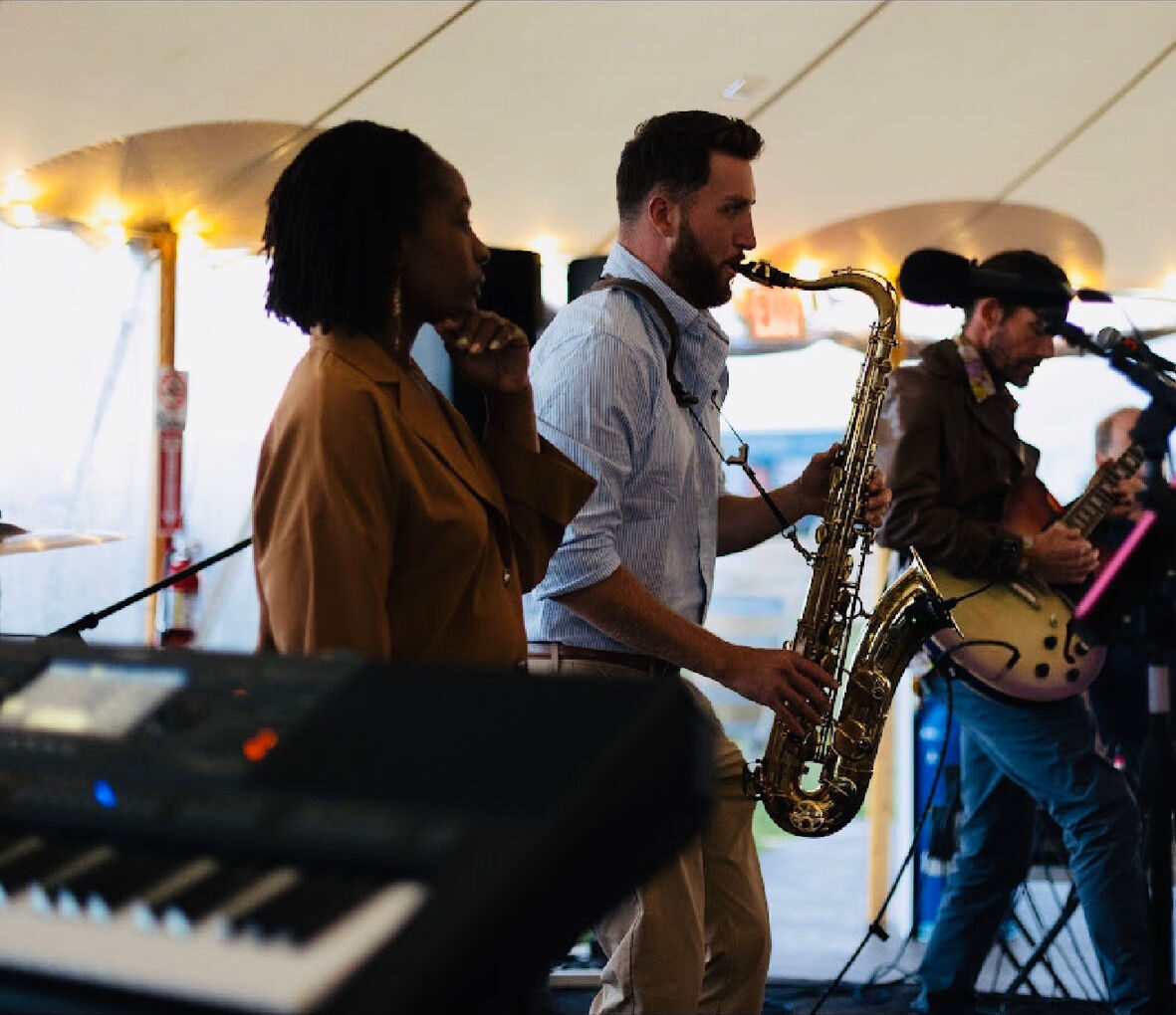 Dawson Bertrand performing saxophone with vocalist and guitarist at a tented event