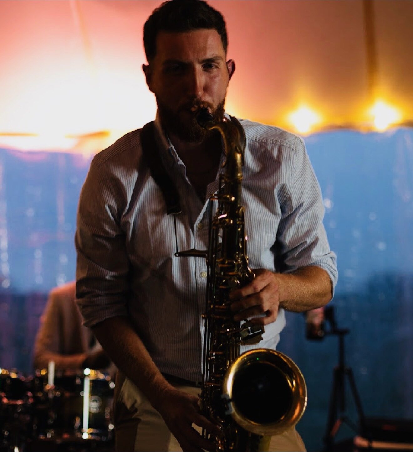 Dawson Bertrand playing tenor saxophone at sunset during a tented reception