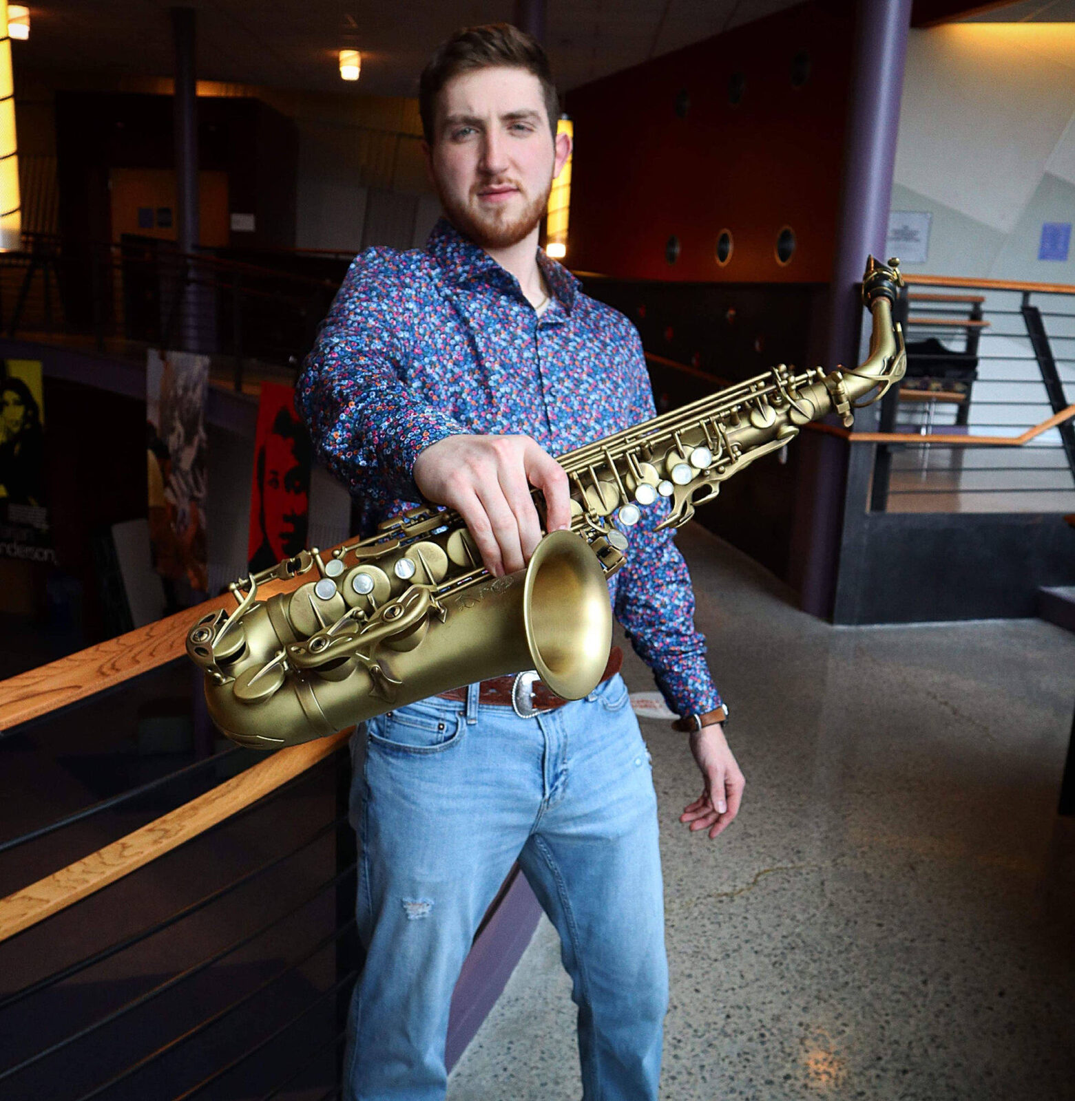 Dawson Bertrand holding a vintage alto saxophone in a theater lobby