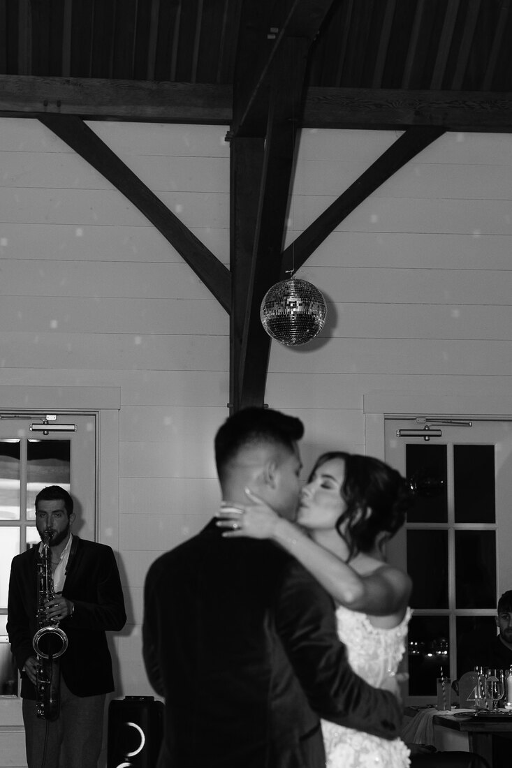 A couple sharing their first dance under a disco ball while Dawson Bertrand plays live saxophone in the background at their wedding reception